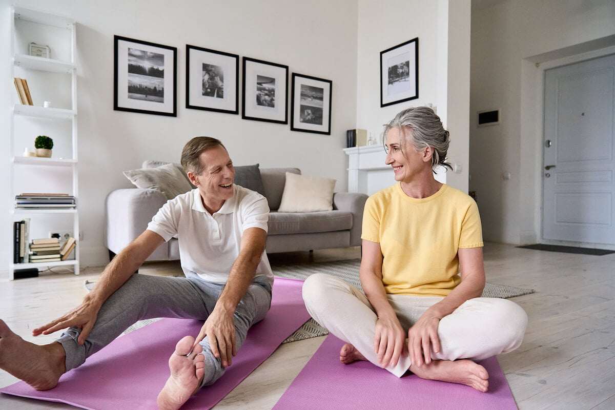 Older man and woman working out together, sitting on yoga mats, indoor workouts