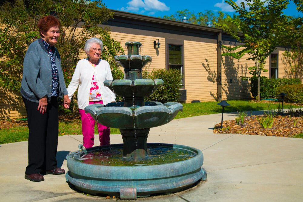 Two Senior Women Holding Hands Stand Beside Fountain_The Pavilion Senior Living