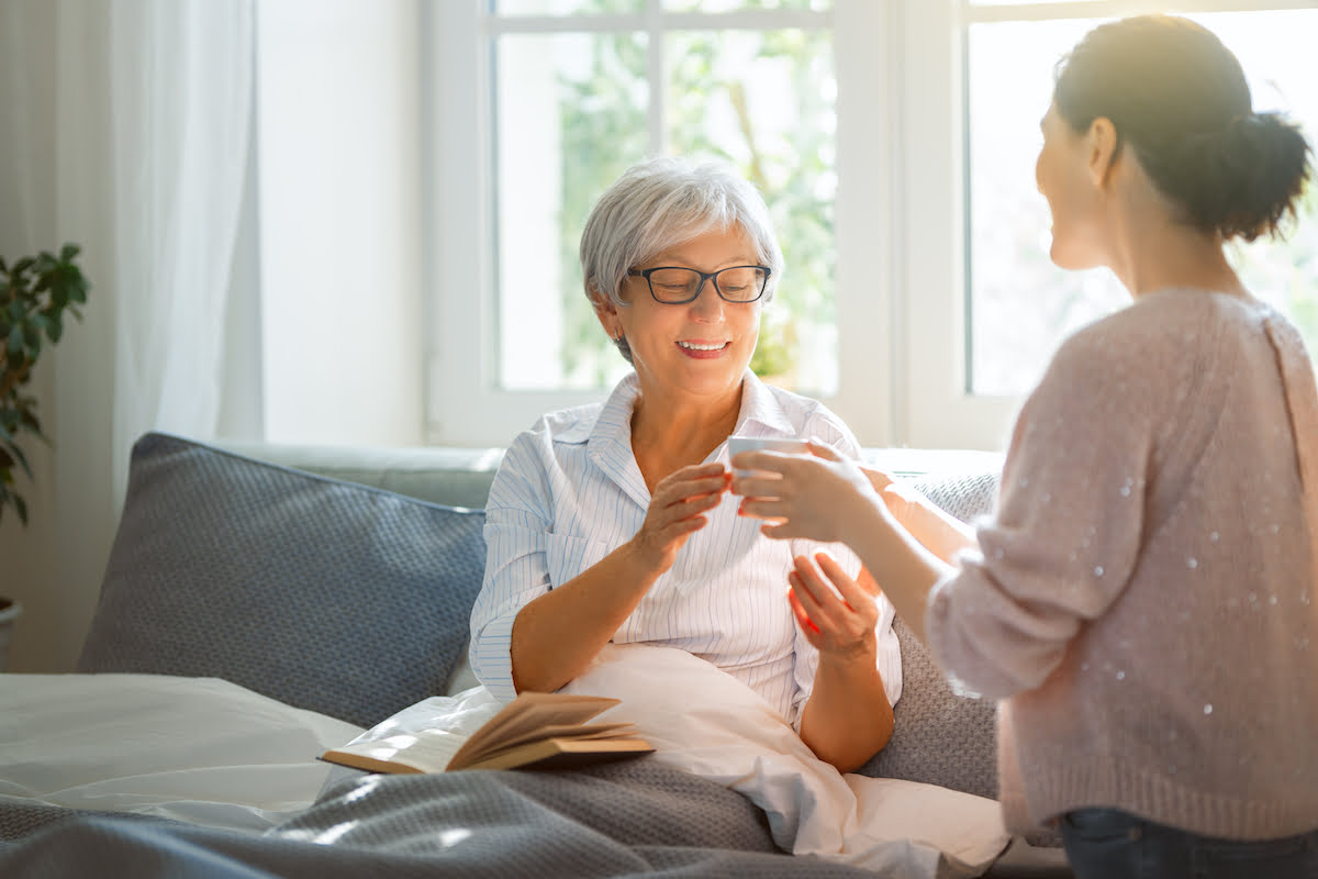 Adult Daughter Hands Coffee Cup to Senior Mother in Bed_The Pavilion Senior Living